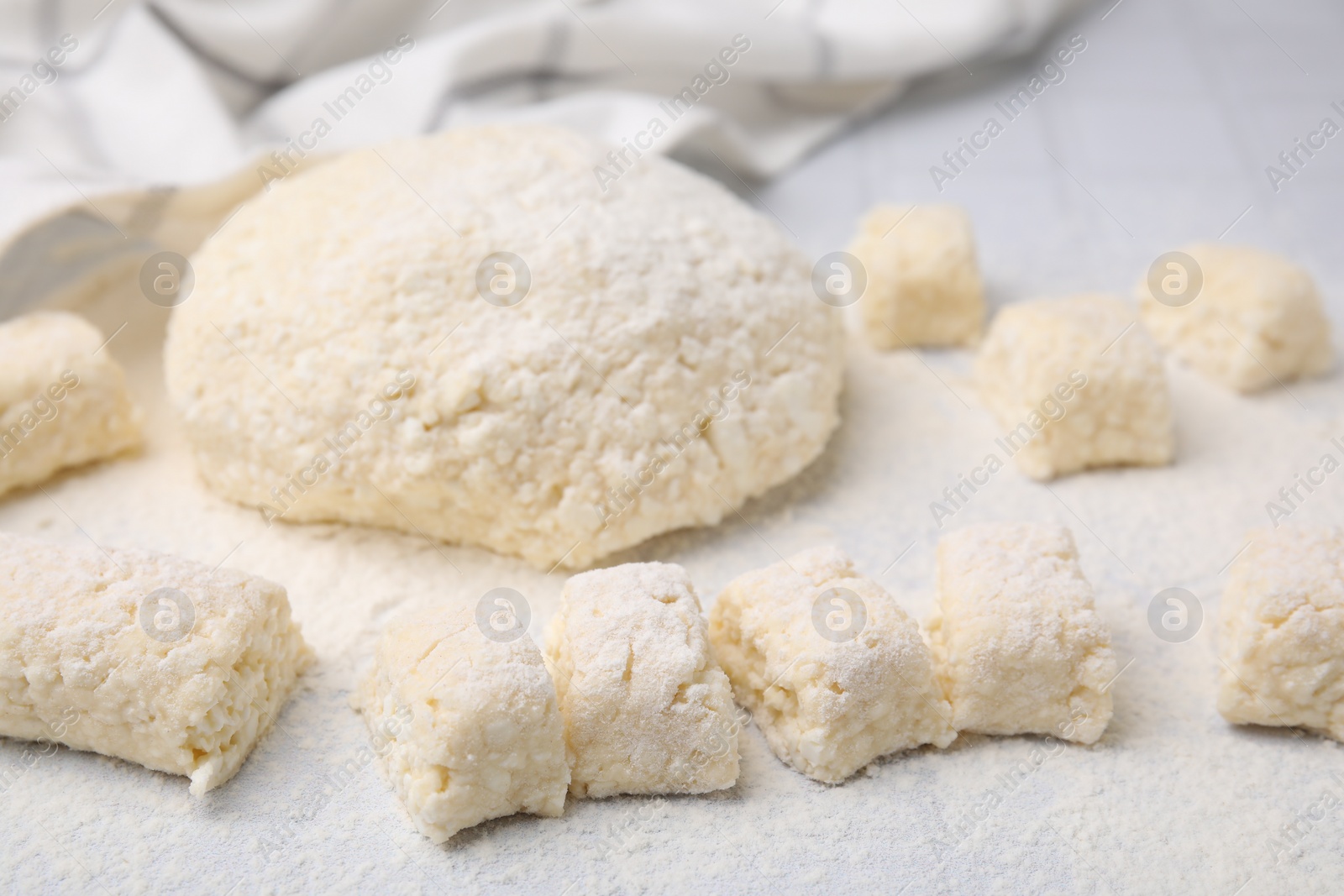 Photo of Making lazy dumplings. Raw dough and flour on white tiled table, closeup