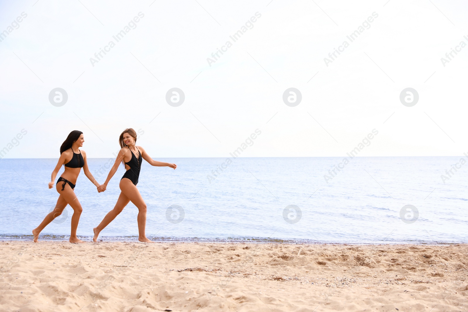 Photo of Young woman in bikini with girlfriend on beach. Lovely couple