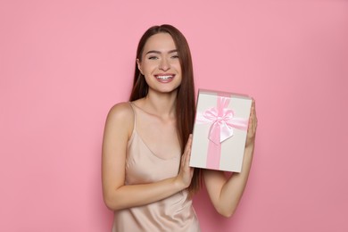 Portrait of happy young woman with gift box on pink background