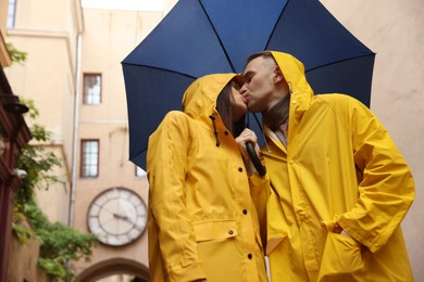 Photo of Lovely young couple with umbrella kissing under rain on city street, low angle view