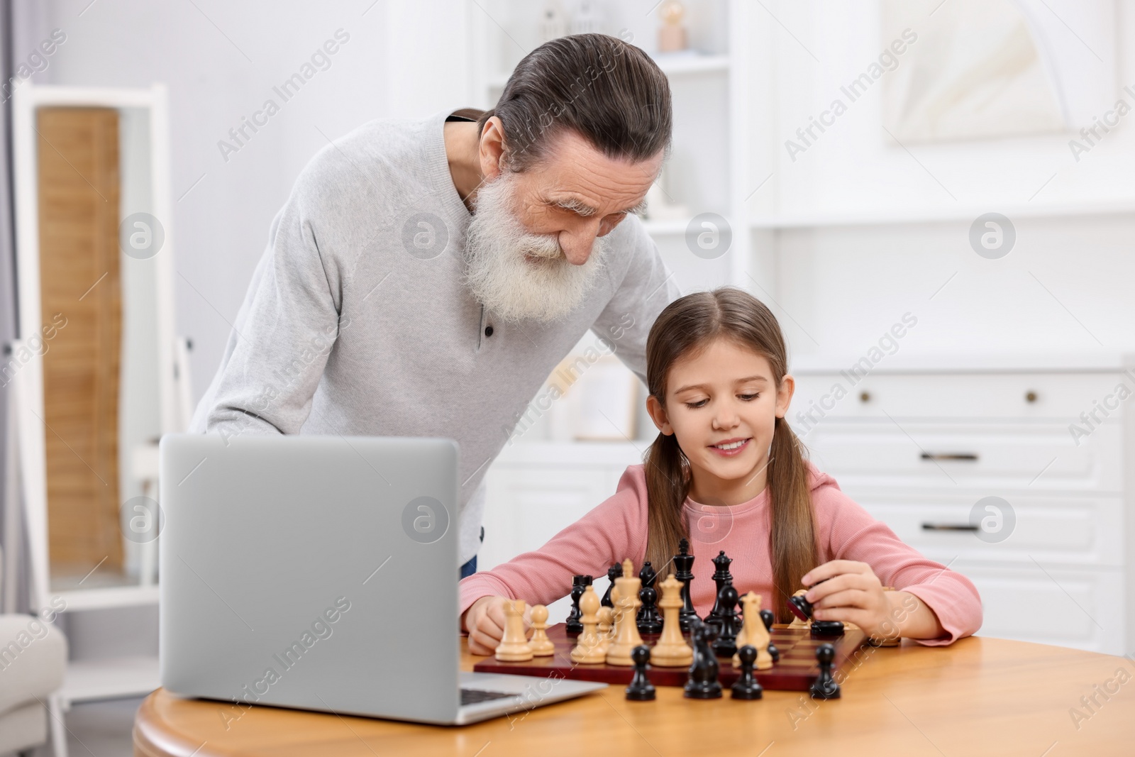 Photo of Grandfather teaching his granddaughter to play chess following online lesson at home