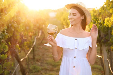 Beautiful young woman with glass of wine in vineyard on sunny day