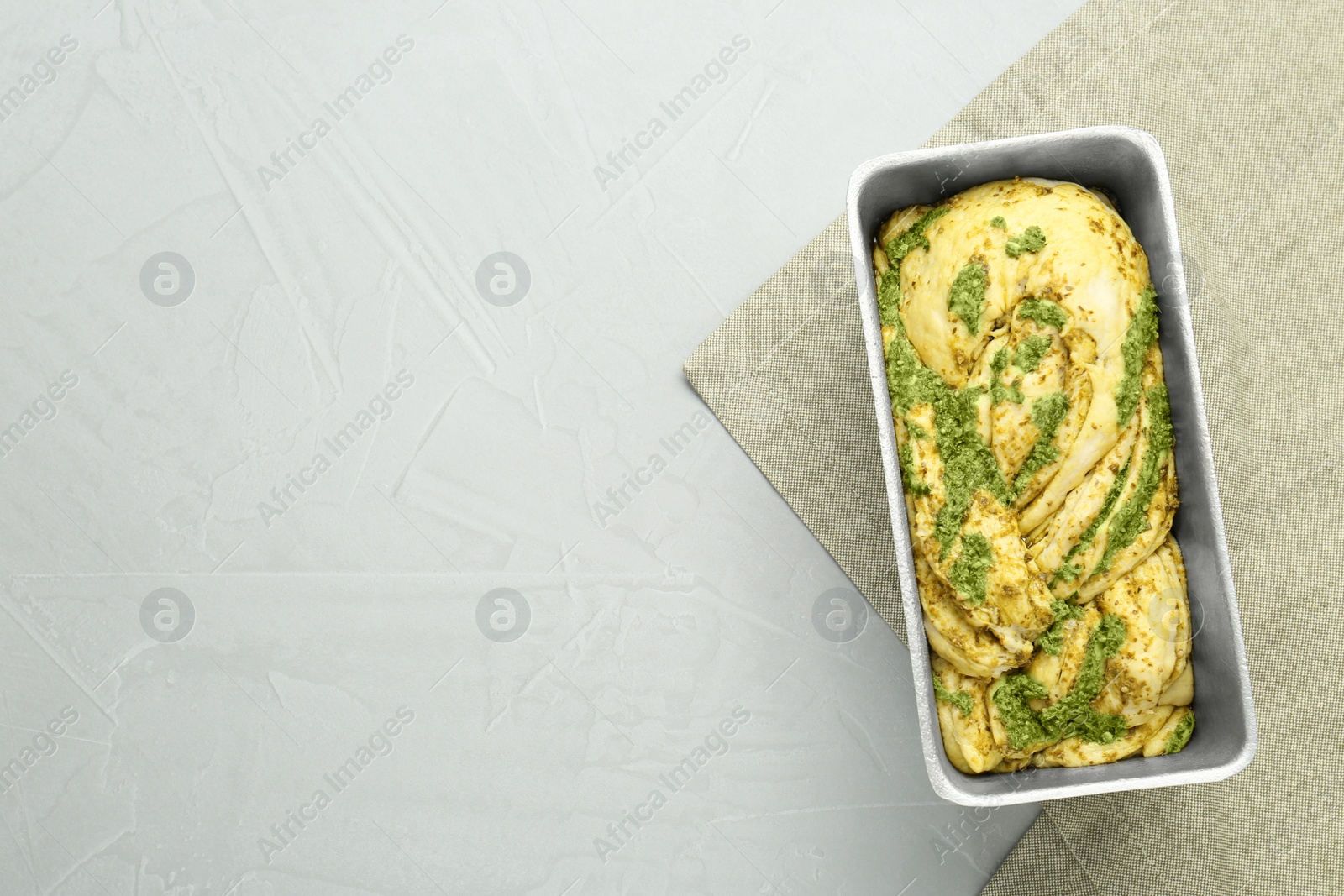 Photo of Uncooked pesto bread in baking dish on light table, top view. Space for text