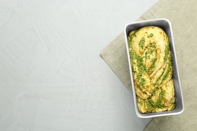 Photo of Uncooked pesto bread in baking dish on light table, top view. Space for text