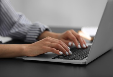Photo of Woman using modern laptop at black desk, closeup