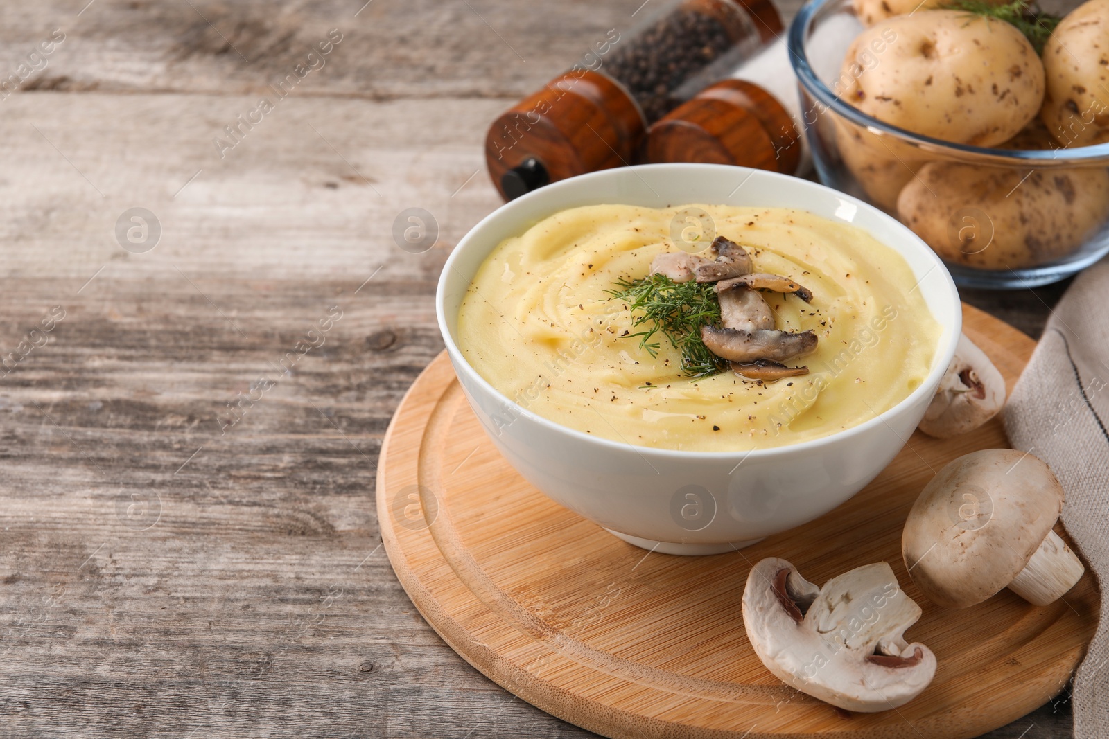 Photo of Bowl of tasty cream soup with fried mushrooms, dill and raw potatoes on wooden table. Space for text