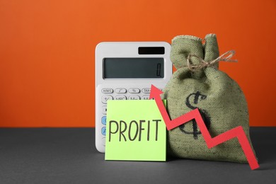 Economic profit. Money bag, calculator, note and arrow on grey table against orange background, space for text