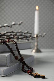 Rosary beads, books and willow branches on white table, closeup