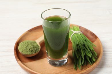 Wheat grass drink in shot glass, spoon of green powder and fresh sprouts on white table, closeup