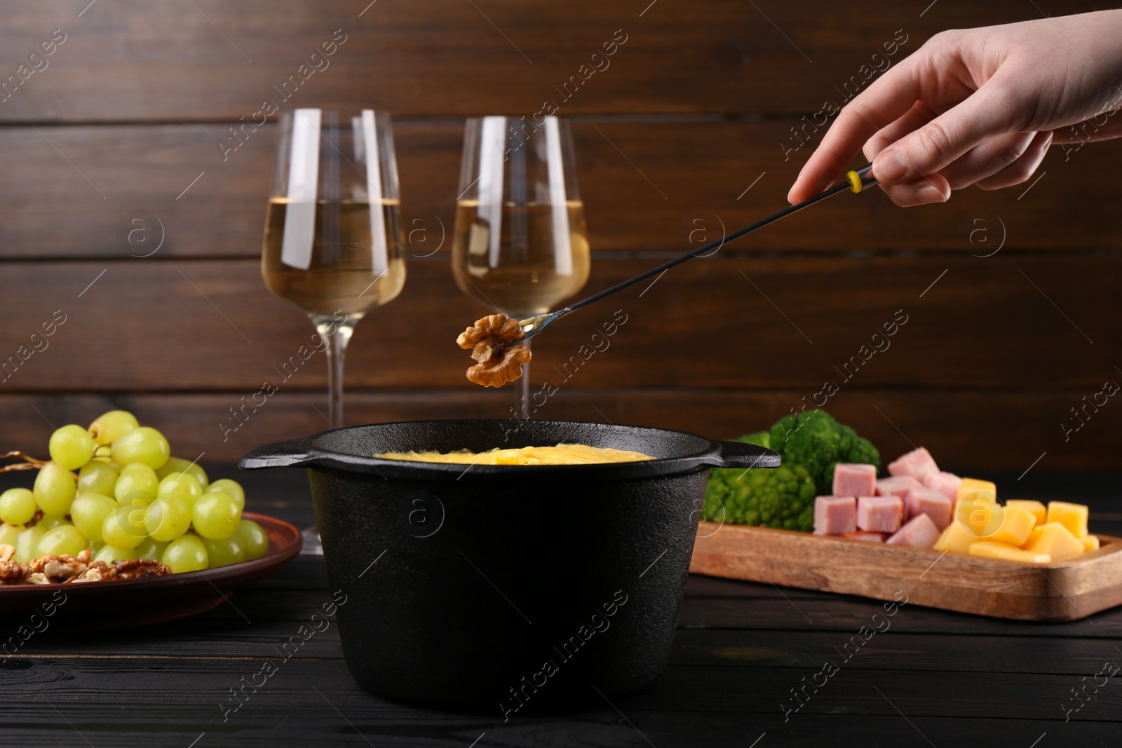 Photo of Woman dipping walnut into fondue pot with melted cheese at black wooden table, closeup