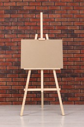 Photo of Wooden easel with blank board near brick wall indoors