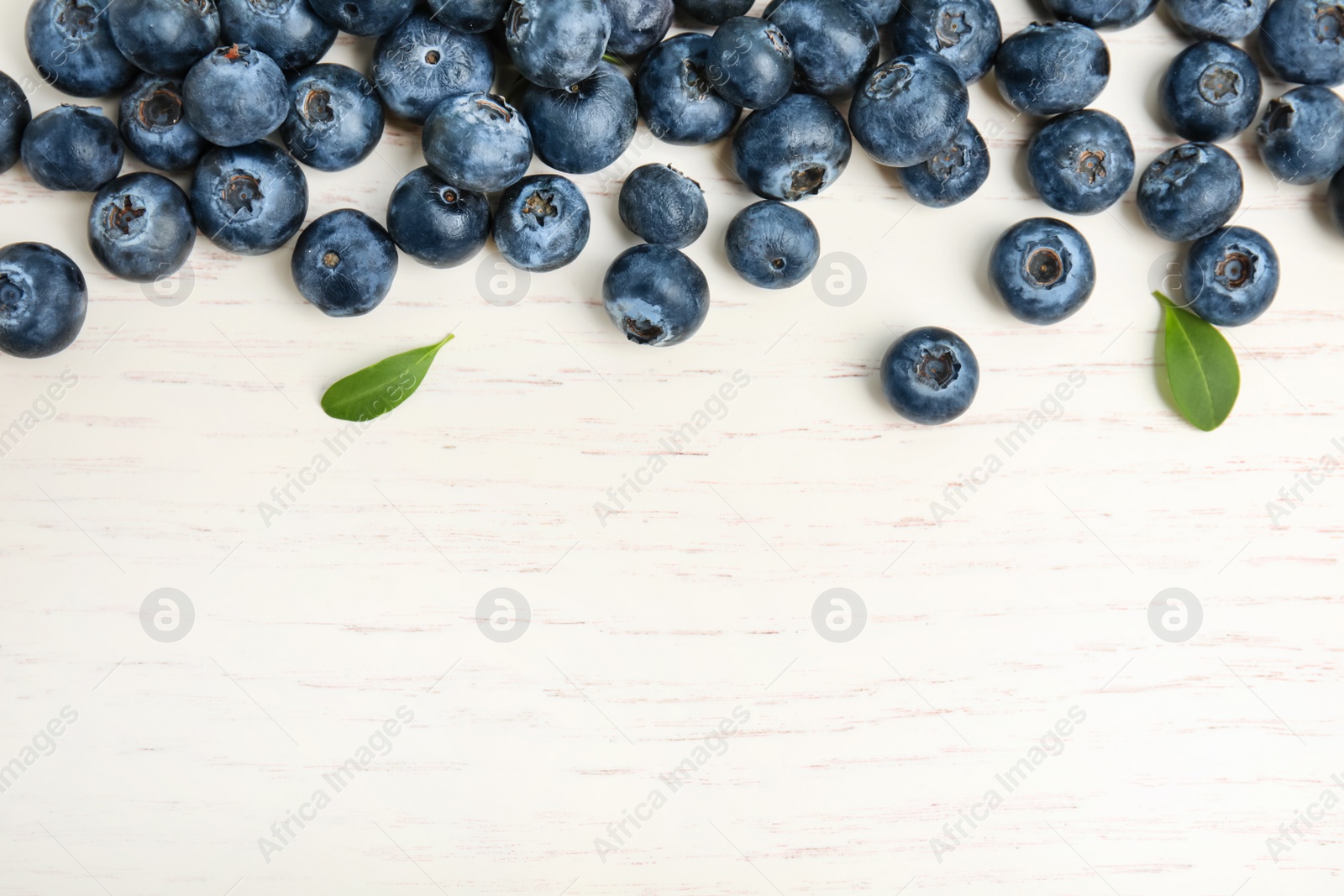 Photo of Fresh ripe blueberries on white wooden table, flat lay. Space for text