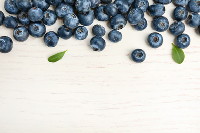 Fresh ripe blueberries on white wooden table, flat lay. Space for text