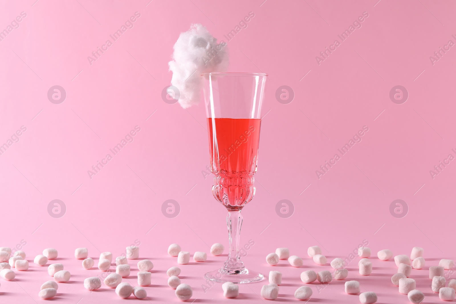 Photo of Tasty cocktail in glass decorated with cotton candy and marshmallows on pink background