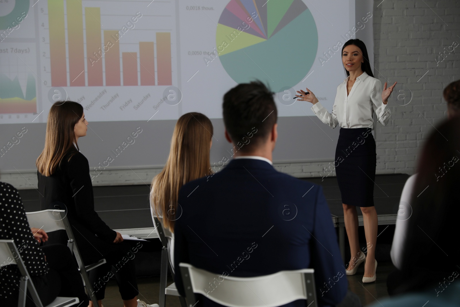 Photo of Female business trainer giving lecture in conference room with projection screen