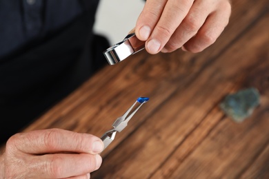 Male jeweler evaluating precious gemstone at table in workshop, closeup