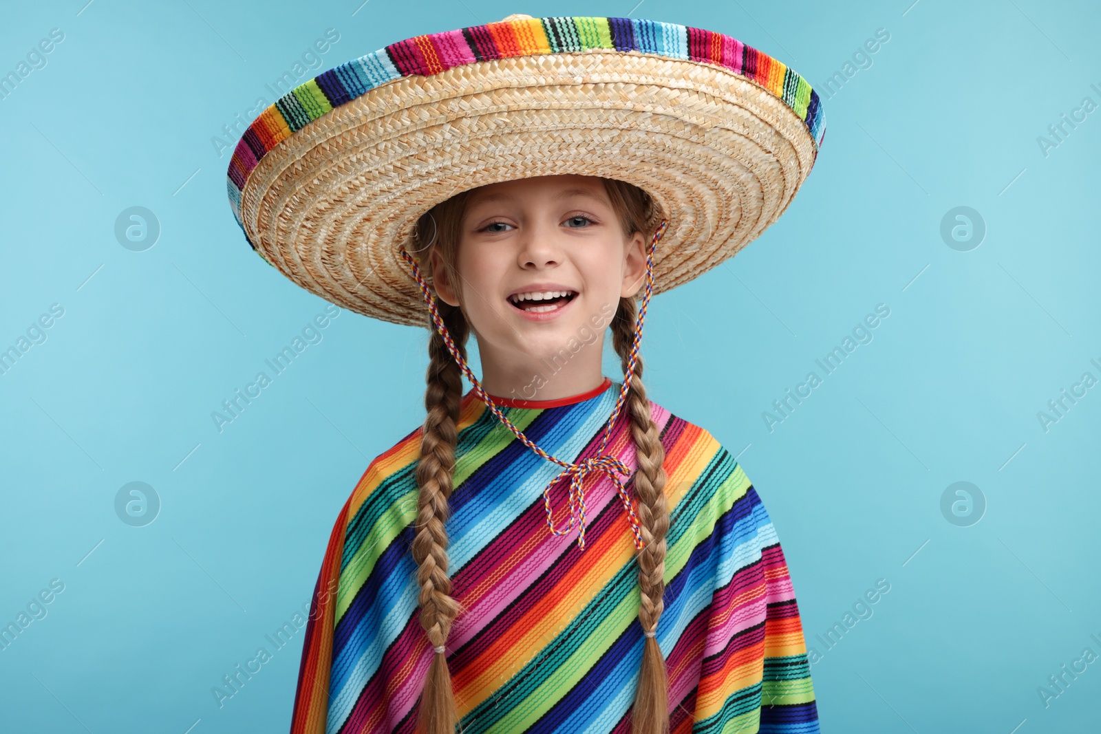 Photo of Cute girl in Mexican sombrero hat and poncho on light blue background