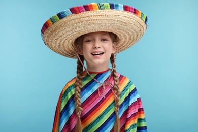 Cute girl in Mexican sombrero hat and poncho on light blue background