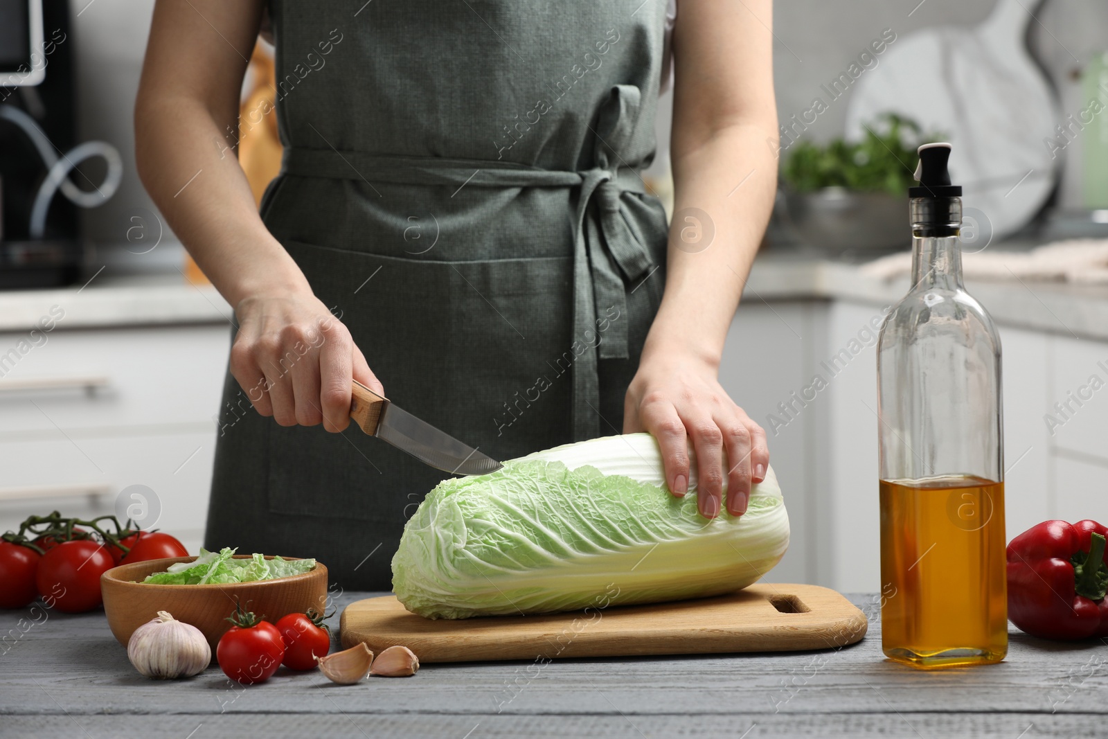 Photo of Woman cutting fresh chinese cabbage at grey wooden table in kitchen, closeup