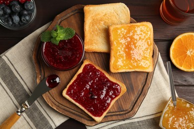 Photo of Delicious toasts served with different jams, tea and fruits on wooden table, flat lay