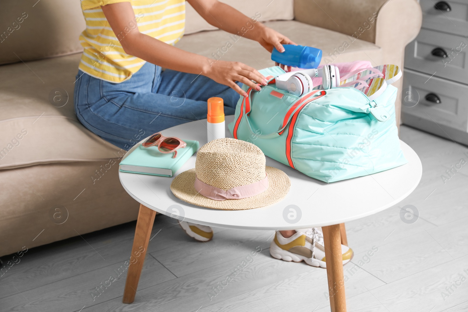 Photo of Woman putting items for vacation in bag indoors, closeup
