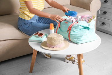Woman putting items for vacation in bag indoors, closeup