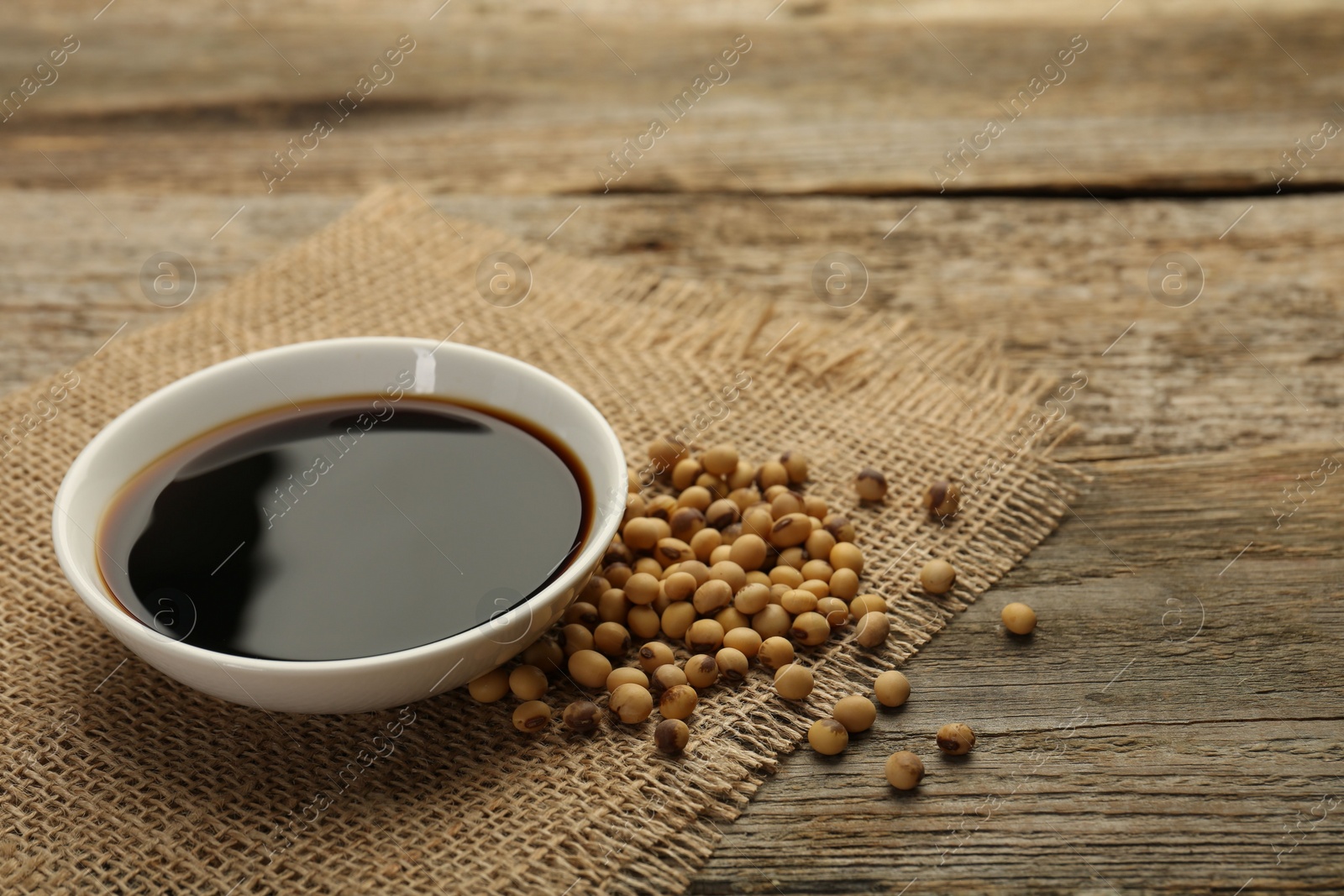 Photo of Soy sauce in bowl and beans on wooden table. Space for text