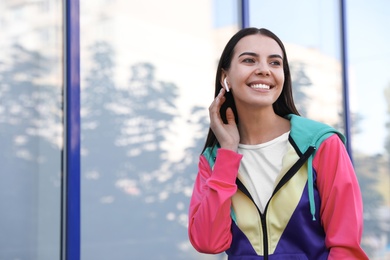 Photo of Young sportswoman with wireless earphones on city street