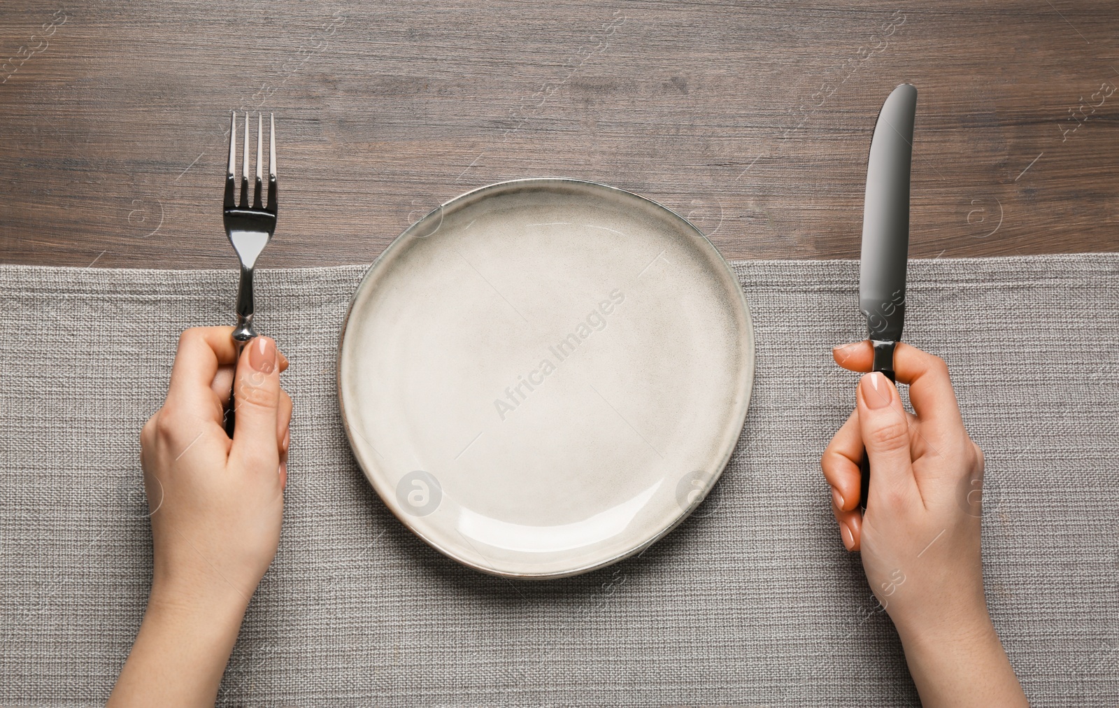 Photo of Woman with empty plate and cutlery at wooden table, top view