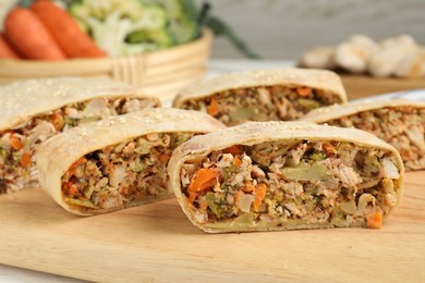 Photo of Cut tasty strudel with chicken and vegetables on wooden board, closeup