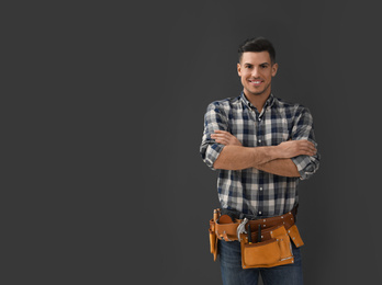 Handsome carpenter with tool belt on dark background. Space for text