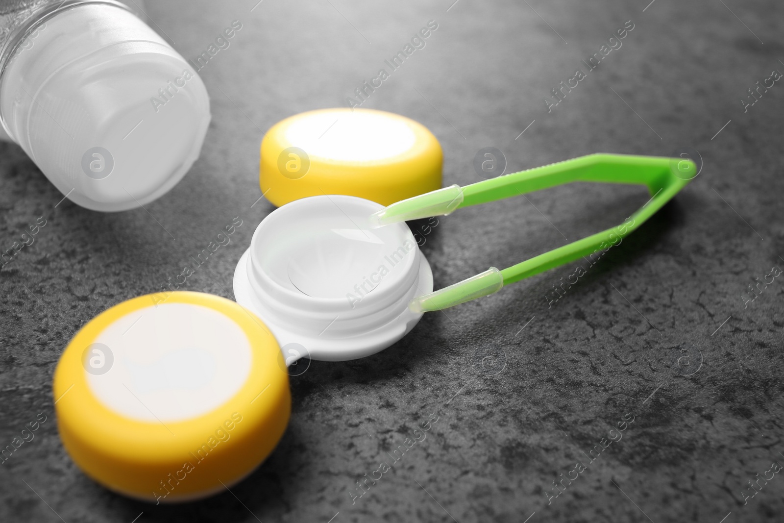 Photo of Container with contact lens and tweezers on table, closeup