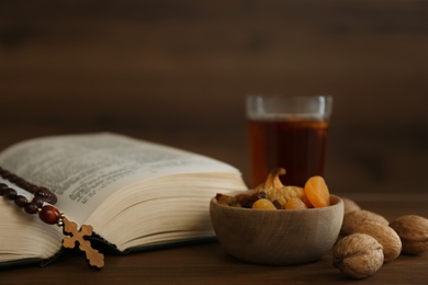 Photo of Bible, rosary beads, walnuts and dried fruits on wooden table. Lent season