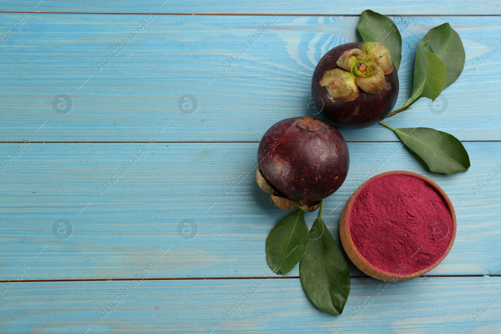 Photo of Purple mangosteen powder and fruits on light blue wooden table, flat lay. Space for text