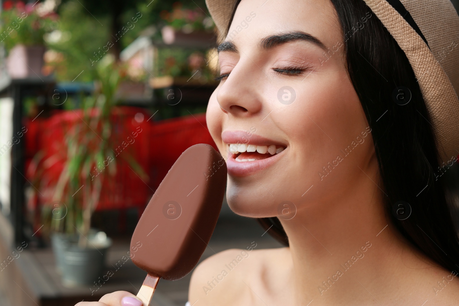 Photo of Beautiful young woman eating ice cream glazed in chocolate on city street, closeup