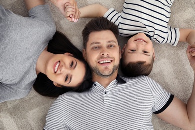 Photo of Happy parents and their son lying together on floor, view from above. Family time