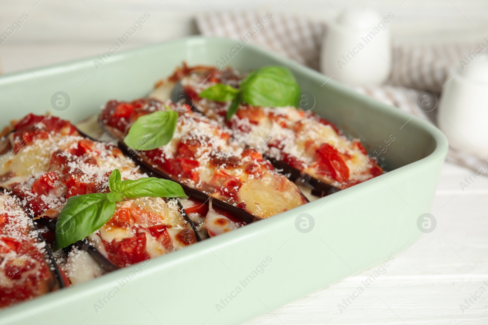 Photo of Baked eggplant with tomatoes, cheese and basil in dishware on white table, closeup