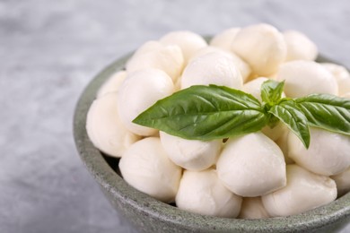 Photo of Tasty mozzarella balls and basil leaves in bowl on grey table, closeup. Space for text