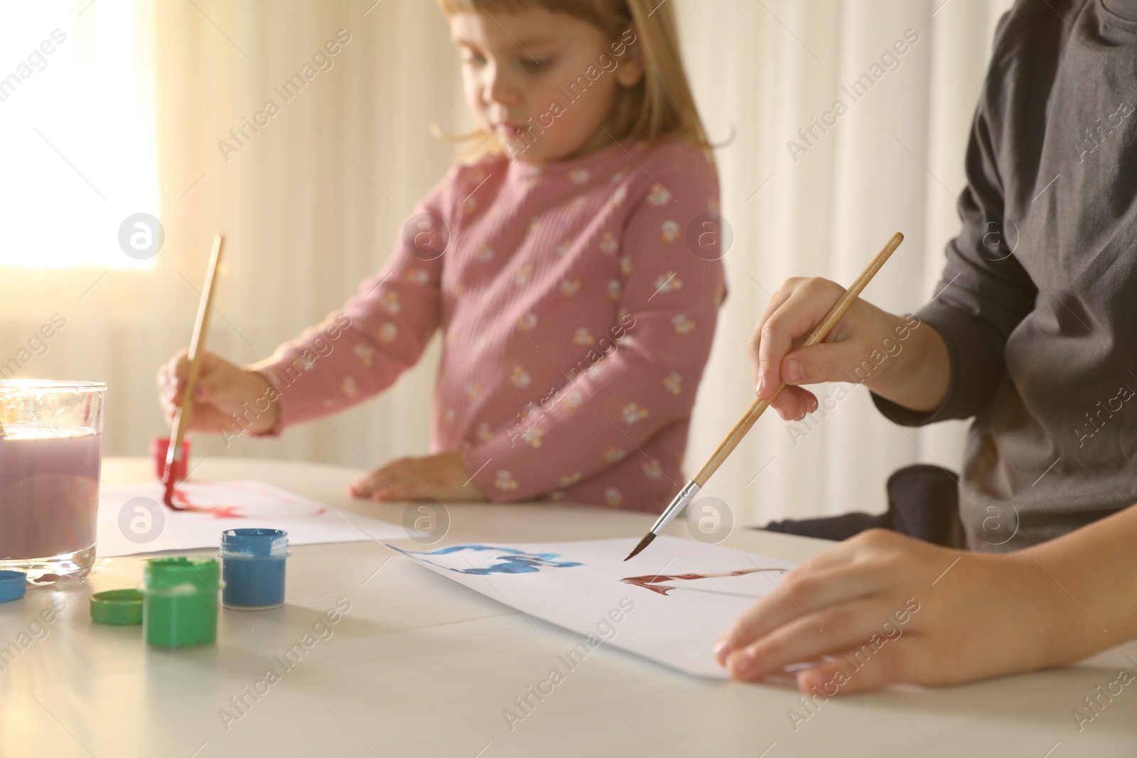 Photo of Little children drawing with brushes at light table indoors, selective focus