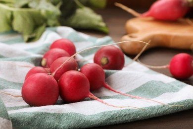 Photo of Towel with fresh ripe radishes on wooden table, closeup