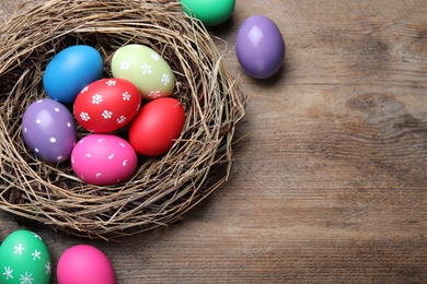 Colorful eggs and nest on wooden background, flat lay with space for text. Happy Easter