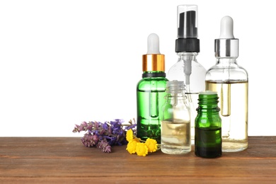 Bottles of herbal essential oils and wildflowers on wooden table, white background