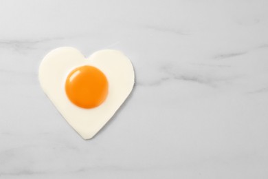 Photo of Heart shaped fried egg on white marble table, top view