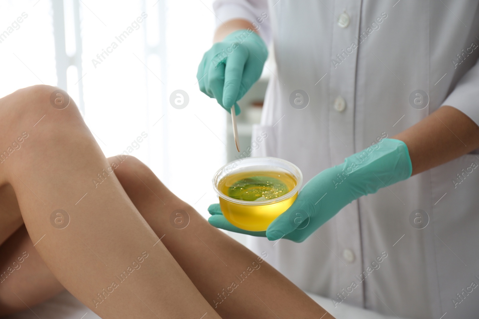 Photo of Woman getting wax epilation of legs in salon, closeup