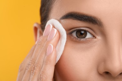 Photo of Beautiful woman removing makeup with cotton pad on orange background, closeup. Space for text