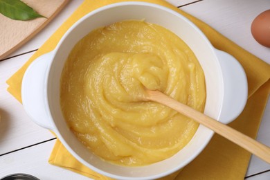 Photo of Delicious lemon curd in bowl and spoon on white wooden table, top view