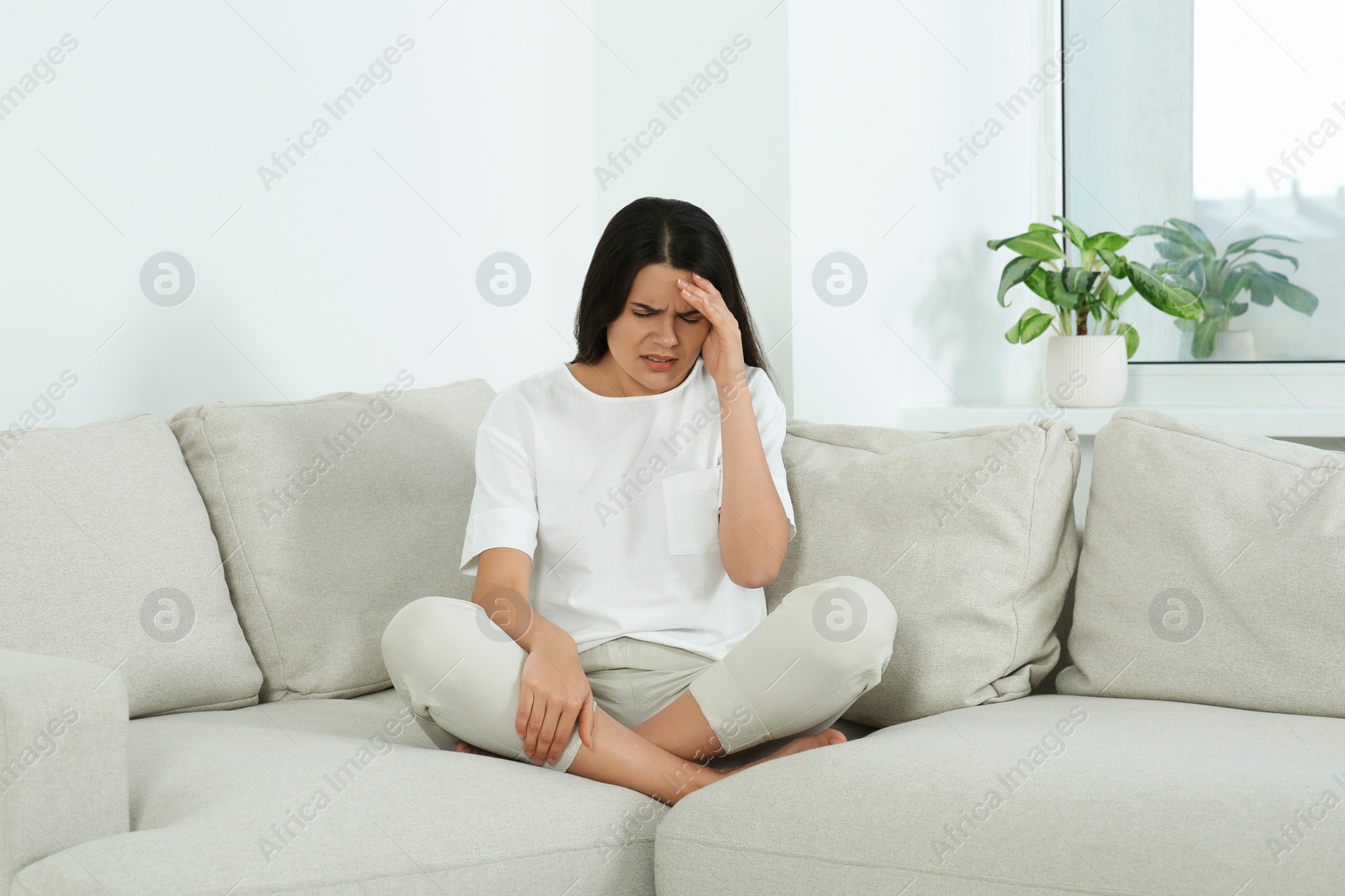 Photo of Young woman suffering from headache on sofa at home. Hormonal disorders