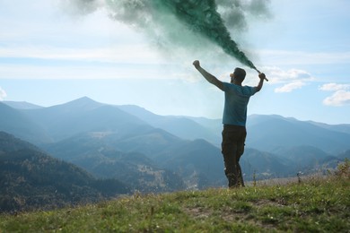 Man holding green smoke bomb in mountains