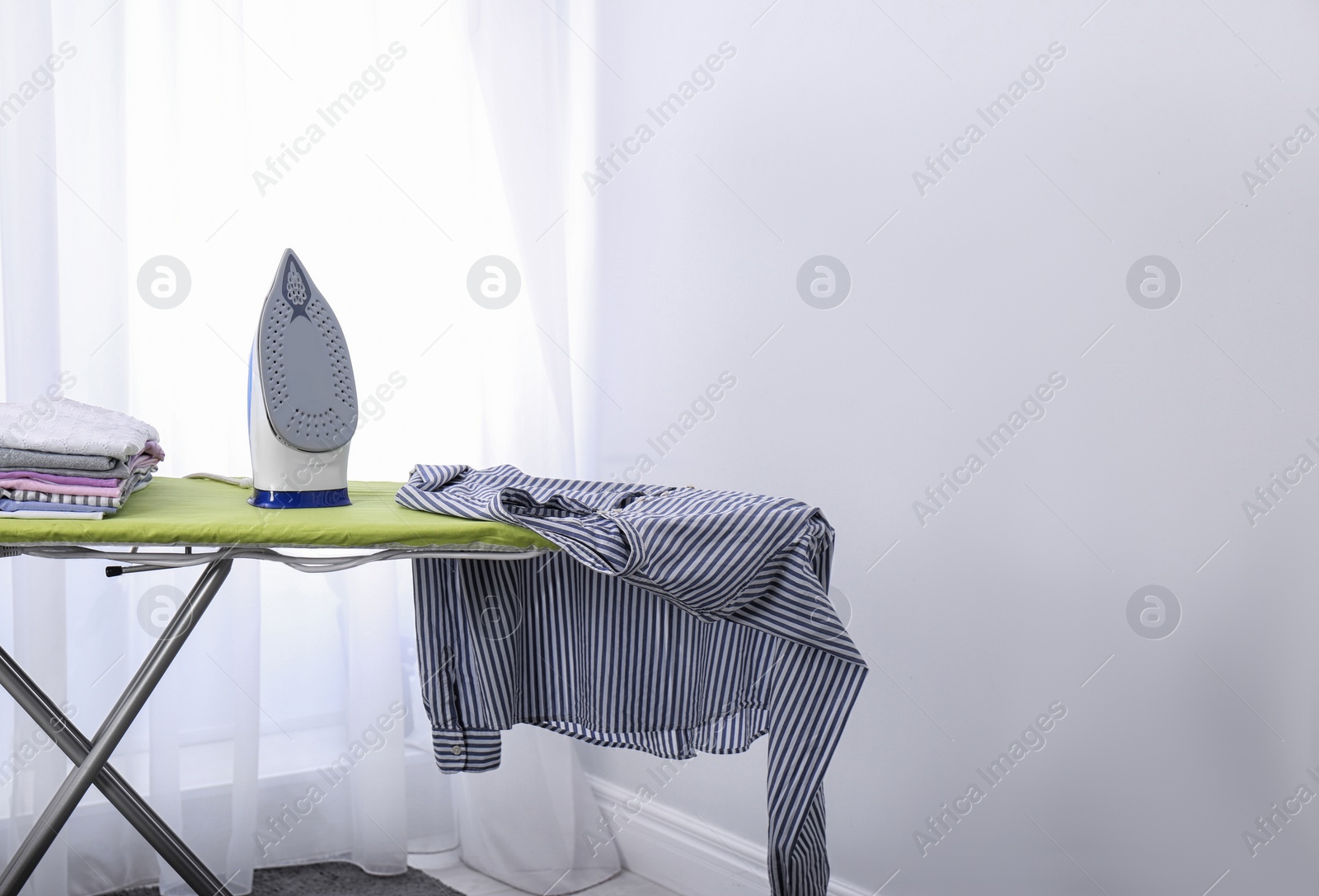 Photo of Modern electric iron and clothes on board  indoors, space for text. Laundry day