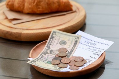 Photo of Tips, receipt and croissant on wooden table, closeup